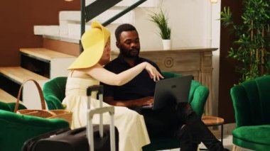 Otel müşterileri dizüstü bilgisayarlarında web sitelerine bakıyorlar, balayı gezisinde eğlenmek için yeni yerler ve boş zaman aktiviteleri arıyorlar. Tropikal tatil beldesindeki dinlenme odasında bekleyen çift..