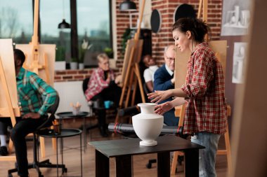 Çeşitli insanlar yerel sanat atölyesinde grup çizimleri sırasında gerçekçi objeler çizmeyi öğreniyor, resim sehpalarında oturuyor ve yaratıcı çizim atölyesinde öğretmenleri dinliyor, yeni beceriler öğreniyor.