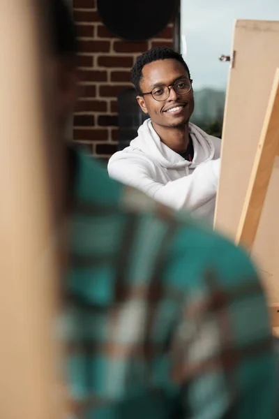Sorrindo Cara Afro Americano Senta Cavalete Desfrutando Atividades Criativas Estúdio — Fotografia de Stock