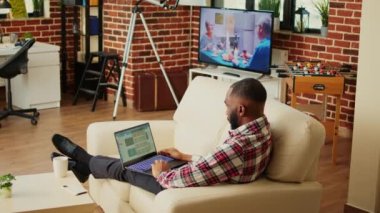 Analitik istatistiksel veri setini kontrol eden telgraf çalışanı, şık bir dairede çalışıyor. İşletme yöneticisi, arka plan gürültüsü olarak TV ile anahtar performans göstergelerini optimize ediyor