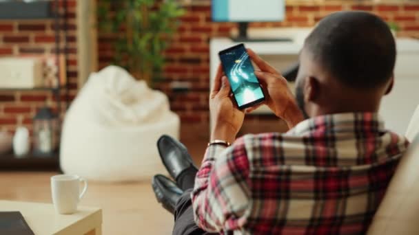 아프리카 미국인 소파에 누워서 스마트폰으로 우주선을 게임을 현대의 아파트에서 너머로 — 비디오