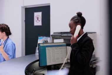 Hastane resepsiyonunda beklerken uzaktan kumandalı bir hastayla tıbbi atamalar hakkında konuşan bir resepsiyonist. Sağlık hizmeti ve konsept