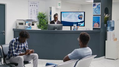 People with disease approaching reception counter to ask about insurance support, talking to receptionist about healthcare. Patients filling in medical report papers before meeting with doctor.