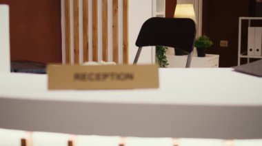 Otel kontrolünden uzaklaşan kamera resepsiyondaki gösterişli lobiye misafirleri karşılamaya hazır. Lüks konaklama salonu, lüks yeşil mobilyaları ve ön masası var.