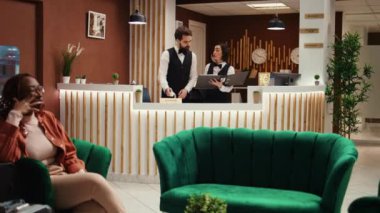 Otel müdürü, uzun bir uçuştan sonra yorgun turistle tatil paketi seçeneklerini ve konfor güncellemelerini tartışmaya hazır. Otel çalışanları misafir odasını hazırlıyor, şık bir resepsiyon salonunda çalışıyor.