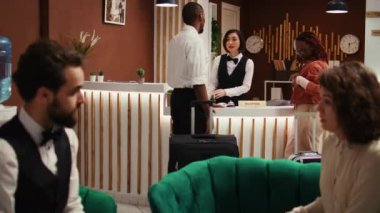Dost canlısı Asyalı resepsiyonist misafirlere rezervasyon için yardım ediyor, onları şık bir otel salonunda beklemeye davet ediyor. Bavullarını taşıyan bellboy 'dan mutlu misafirler.