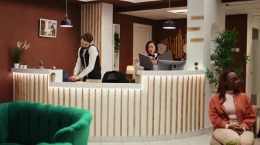 Dost canlısı, neşeli otel yöneticisi, ziyaretçi geri bildirimi alıyor, kontrol sürecinde kaldıkları süreyi soruyor. Resepsiyonda çalışan otel çalışanları.