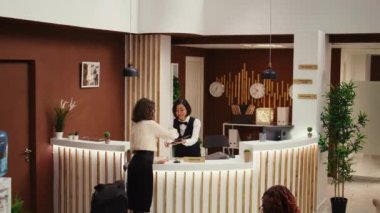 Tablete imza atan otel ziyaretçisi ve kontrol sırasında Asyalı arkadaş canlısı resepsiyonist tarafından oda giriş kartı verilmesi. Konsiyerj personeli otel lobisinde misafirlere yardım ediyor.