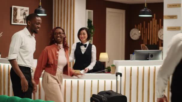 快乐的非洲裔美国游客在度假胜地大堂给提行李的侍者小费 在把房间出入卡交给友好的接待员后 愉快的客人从酒店退房 — 图库视频影像