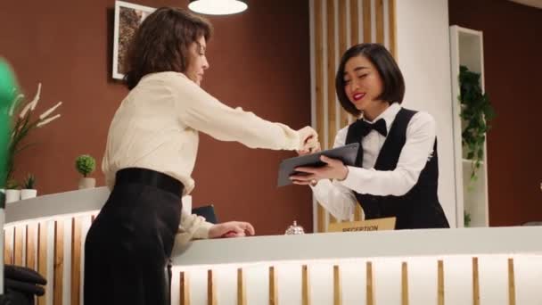 チェックインの際 ホテルのゲストはタブレットで署名を書き アジアの受付担当者がルームカードキーを渡すことができます リゾートラウンジの観光客を助けるチームワークコンシェルジュスタッフ — ストック動画