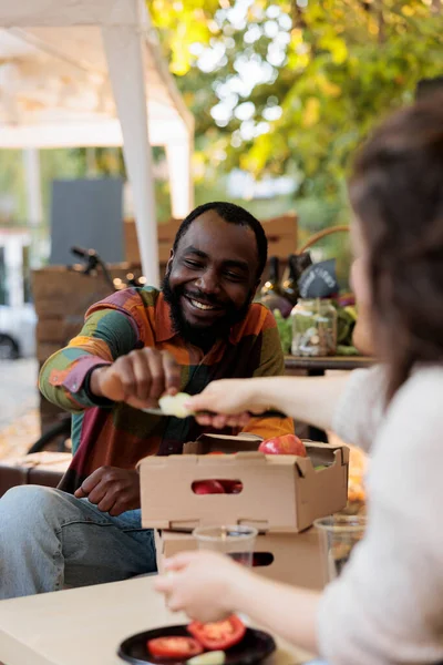 快乐的非洲年轻人顾客在农贸市场品尝有机水果和蔬菜 笑着和当地供应商一起坐在桌旁寻找苹果品种 同时参观食品展销会 — 图库照片