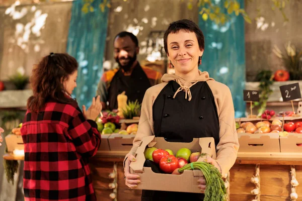 快乐的女农民在当地市场上销售有机农产品 健康受益于当地种植的食品 满满一盒新鲜的季节性水果和蔬菜 微笑着站在卖主的架子上 — 图库照片