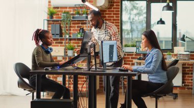 Team of diverse colleagues developing digital software in production studio, working with creative interface and artificial intelligence. Professional people creating virtual infographics.