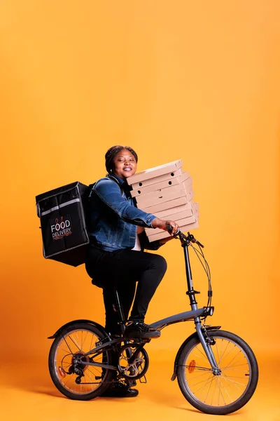 Restoran Işçisi Bisiklet Sürerken Pizza Paketini Sarı Arka Planlı Stüdyoda — Stok fotoğraf
