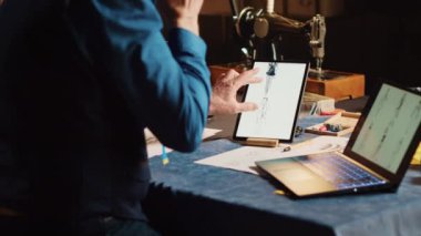 Erkek terzi, atölyedeki aletleri kullanarak çizimlerdeki öğeleri kontrol ederek el yapımı modern giyim markası oluşturuyor. Moda tasarımı için terzilik işinde deneyimli bir zanaatkar. El kamerasıyla..