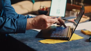 Erkek terzi, dizüstü bilgisayarında kredi kartıyla kumaş alıyor. Lüks kıyafetler için malzeme ve tekstil endüstrisi aletleri alıyor. Atölyede daha şık. El kamerasıyla. Kapat..