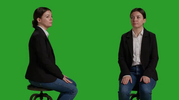 Close up of female manager waiting on chair before corporate meeting, sitting in studio with greenscreen background. Woman dressed in office suit working as employee or businesswoman.