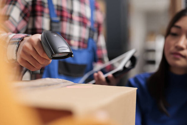 Freight distribution center employee using barcode scanner in warehouse. Logistic manager scanning cardboard box qr code while supervising goods receiving and sending operations