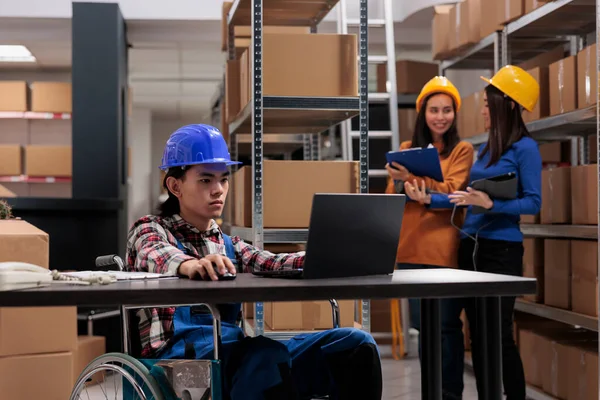 坐在轮椅上的亚洲仓库员工在笔记本电脑上对商品库存进行优化 邮政服务发货操作员在方便残疾人的仓库的计算机桌旁工作 — 图库照片