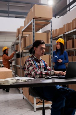 Lojistik müdürü, nakliye deposunda dizüstü bilgisayardan mal tedarik etmeyi planlıyor. Genç Asyalı sevkiyat elemanı bilgisayarda yazıyor ve depodaki envanter yönetim sistemini kontrol ediyor.