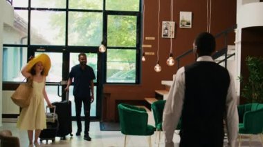 Misafirler için bavul taşıyan otel kapıcısı lobide turistlere lüks komi hizmeti sunuyor. Afrika kökenli Amerikalı komi ön masaya gelen bir çift için tramvay çantası alıyor. El kamerasıyla..