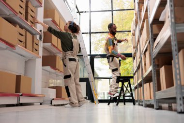 Depo çalışanı karton kutu detaylarını analiz ediyor, depolama odasındaki müşteriler için mal teslimatında çalışıyor. Depo yöneticisi kulaklık takıyor. Ürün hazırlarken müzik dinliyor.