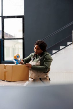 İşçi karton kutulara yapışkan bant yapıştırıyor, müşterilerin siparişlerini depoda hazırlıyor. Afro-Amerikan depo çalışanı teslimattan önce paketleri kontrol ediyor, depo envanterinde çalışıyor.