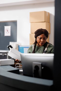 Beyaz karton kutu tutan Afrikalı Amerikalı bir yönetici müşterilerin siparişlerini depoda nakliye için hazırlıyor. Envanter odasında çalışan endüstriyel giyimli küçük işletme işçisi.