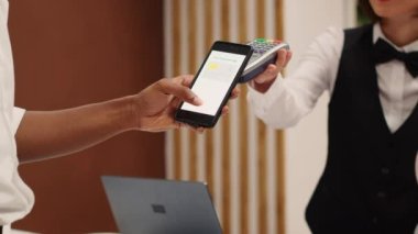 Akıllı telefon bankacılığı uygulaması kullanarak kontrol sırasında oda güncellemesi için Afrikalı Amerikalı turistleri kapatın. Kredi kartı alımını onaylamak için POS ödeme terminalini kullanan resepsiyonist
