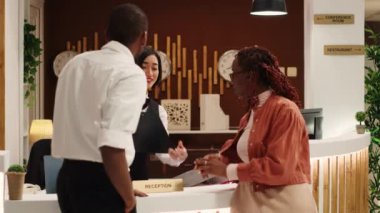 Asyalı resepsiyonist, Afrika kökenli Amerikalı turistlerin tatil paketini yeniledikten sonra imzalamaları için tabletle kontrat veriyor. Lüks otelde balayı gezisi yapan mutlu misafirler.