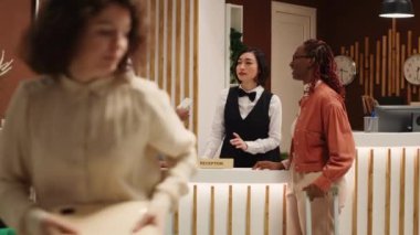 Yorgun otel konukları, uzun bir uçuştan sonra odalarında kontrol edilmeye hazır Asyalı resepsiyonistten giriş kartı alıyorlar. Profesyonel komi, turistlere bagajlarında yardım ediyor.
