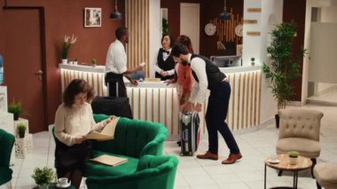 Konsiyerj personeli onlara yardım ederken turistlerin evrak işlerini hallettiğini onaylayan odaklı otel müdürü. Bellboy konuklara bavul taşımada yardım ediyor..