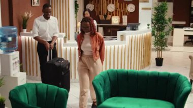 Resepsiyonist, balayı gezisinde turistlere rezervasyon için yardım ediyor. Mutlu yeni evli çift odalarında kontrol edilmeye hazırlar, otel odasında bellboy bagajlarını alırken bekliyorlar.