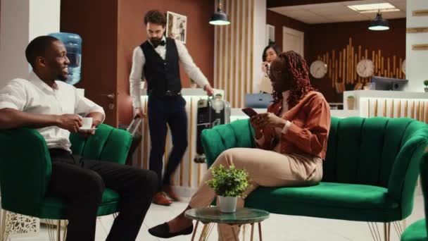 在新婚夫妇度蜜月的途中 他们在时尚宾馆的休息室里享受着一杯咖啡 等待在他们的房间里检查 非洲裔美国游客在度假胜地大堂讨论有趣的短信 — 图库视频影像