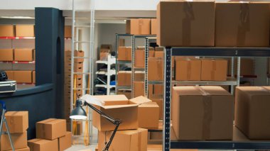 Storage room area filled with products packed in boxes, placed on shelves and racks in empty storehouse. Small business space used for shipping merchandise and doing stock inventory.