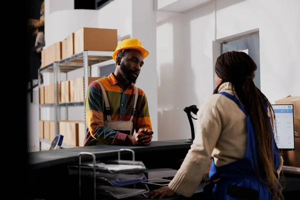 出荷管理を議論カウンターデスクに立つ倉庫労働者 アフリカ系アメリカ人の郵便局の従業員2人が保管室のチェックアウト時の荷物配達について話しています — ストック写真