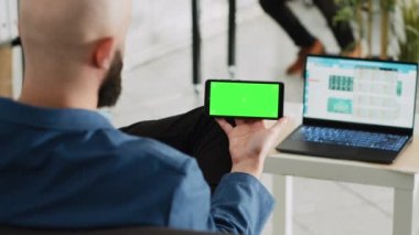İşçi yeşil ekran ekranına bakıyor, küçük işletme planı için araştırma yapmaya hazırlanıyor. Ayrı bir kopyalama alanı ve açık ofis alanı olan akıllı telefon tutan genç..
