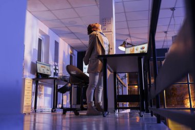 Şirket stratejisinde fazla mesai yaptıktan sonra ayakta duran ve boynunu uzatan yorgun girişimci, başlangıç ofisindeki mali grafik raporunu analiz ediyor. Şirket işçisi yatırım planı