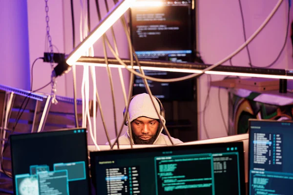 画面上の違法コードを持つ複数のコンピュータモニタ上のヘッドフォンプログラミングマルウェアのハッカー アフリカ系アメリカ人の男がデータベースとハッキングネットワークシステムに侵入 — ストック写真