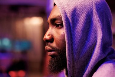 Kapüşonlu konsantre Afro-Amerikan adam karanlık odada bilgisayar sistemine giriyor. Odaklanmış genç bilgisayar korsanı internet virüsü ve fidye virüsü saklanıyor ve neon ışığı kapalı.