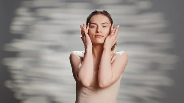 Confident woman using moisturizing facial cream for beauty routine, creating new ad campaign for glowing products. Cheerful sensual girl posing on camera to advertise nourishing luminous look.