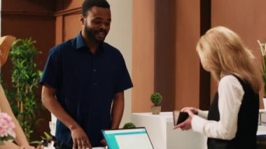 Egzotik deniz kıyısındaki tatil beldesinde turistleri kaydettirmek için pasaportlara bakan resepsiyonist, balayı gezisinde çiftlerle konuşuyor. Otel müşterileri resepsiyondan kontrol ediyorlar. El kamerasıyla..