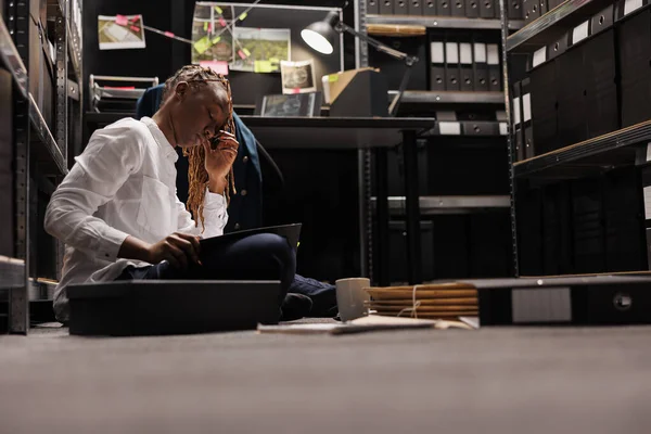 一个疲惫的女警察晚上坐在侦探办公室的地板上加班 过度劳累的调查员阅读犯罪学专门知识报告和揉揉眼睛 — 图库照片