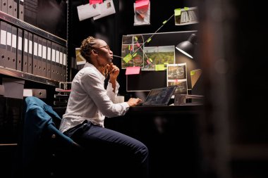 Ajans odasındaki bilgisayardaki güvenlik kamerası görüntülerine bakan özel dedektif kadın. Çalışma masasında çalışan bir müfettiş, bilgisayar kullanıyor ve şüphelileri gözetliyor.