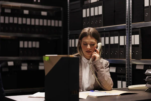 簿记员使用固定电话与经理讨论会计报告 在储藏室的管理研究中加班 留任员工查核官僚记录 — 图库照片