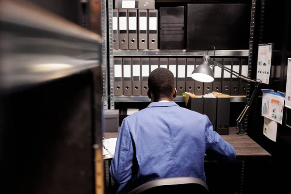 簿记员坐在储藏室的办公桌前 为官僚记录工作 阅读带有行政报告的档案 非裔美国人经理分析公司托存处的会计文件 — 图库照片