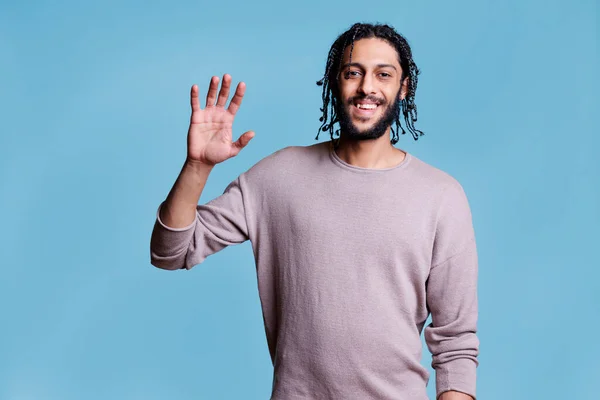優しい笑顔のアラブ人男性がこんにちは手を振って 肯定的な感情を持つカメラを見て 朗らかなアラビアのハンサムなモデルを身に着けているカジュアル服のための手を上げるための挨拶肖像画 — ストック写真