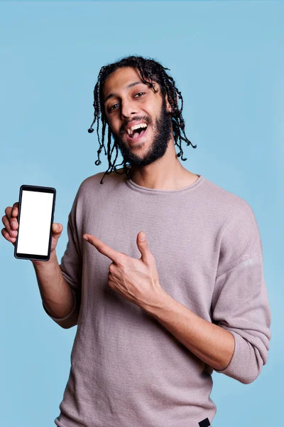微笑的Arab男人展示手机与白色屏幕的应用广告和相机 兴高采烈的广告主 用手指指指智能手机 空显示文字 — 图库照片