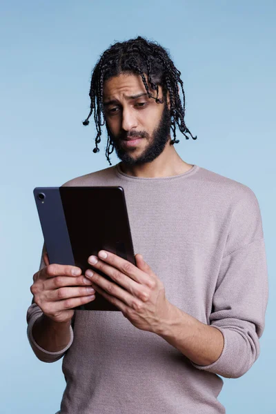アラブ人男性はオンラインでメッセージを読み デジタルタブレットでソーシャルメディアをスクロールします 携帯用ガジェットソフトウェアアプリながらカジュアルな服のテキストメッセージやサーフィンインターネットを身に着けている若い人 — ストック写真