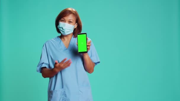 Pielęgniarka Masce Ochronnej Pokazuje Film Instrukcją Medyczną Zielonym Ekranie Telefonu — Wideo stockowe